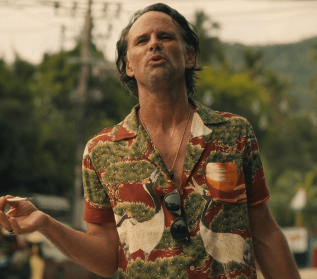 Rick Hatchett embodies a laid-back vacation aesthetic in a vibrant, short-sleeved button-up shirt, its distinctive pattern a nod to tropical escapism. The open collar and casually hung sunglasses complete a look perfectly suited for sun-drenched days.