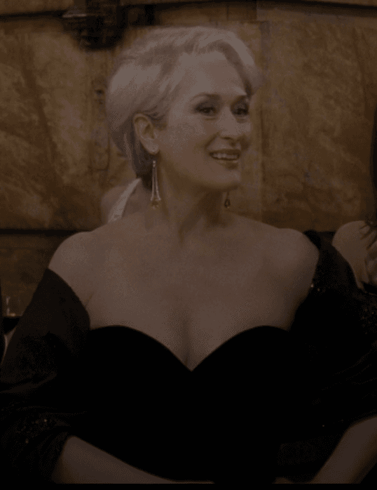 Miranda Priestly captivates in a sophisticated black strapless gown, exuding an air of effortless authority and elegance at a high-profile evening affair. The sweetheart neckline and shimmering wrap perfectly frame her iconic silver coiffure and radiant smile.