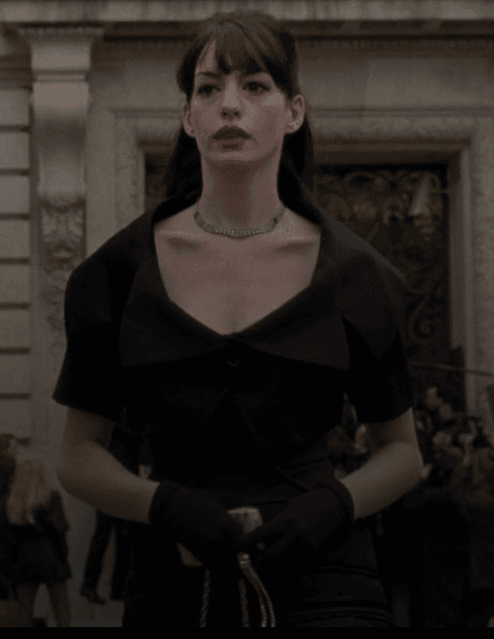 Andy Sachs embodies a chic transformation, poised in a sophisticated black bolero with a dramatic collar, paired with elegant long gloves and a sparkling choker, signaling a confident step into the high-fashion world.